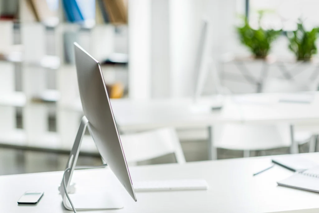 Moderner, heller Büroarbeitsplatz mit großem Monitor auf einem weißen Schreibtisch.