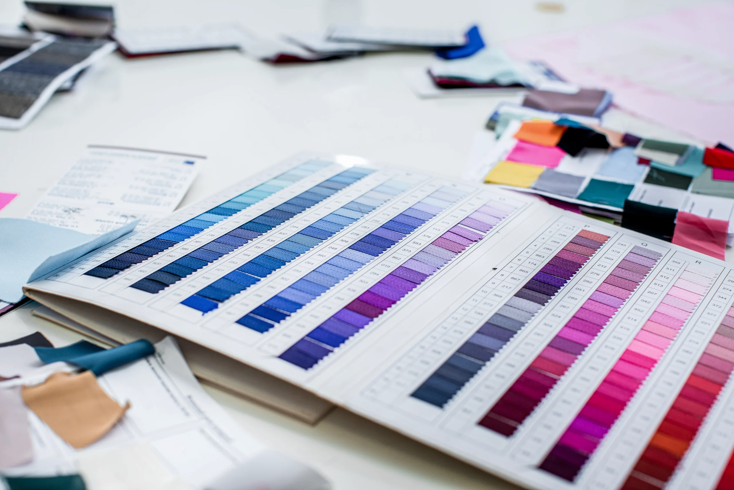 Offenes Farbmusterbuch mit Stoffproben in Blau-, Lila- und Pinktönen, umgeben von weiteren Farb- und Materialmustern.