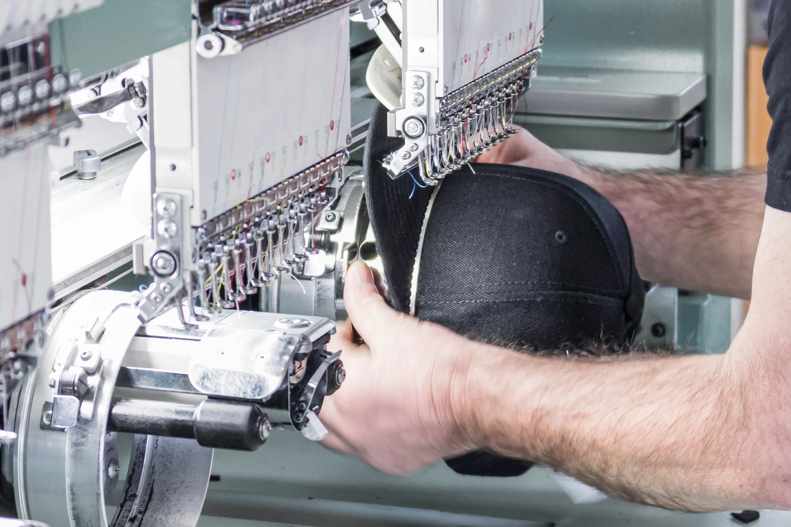 Mitarbeiter spannt eine schwarze Cap in eine industrielle Stickmaschine zur Veredelung ein.